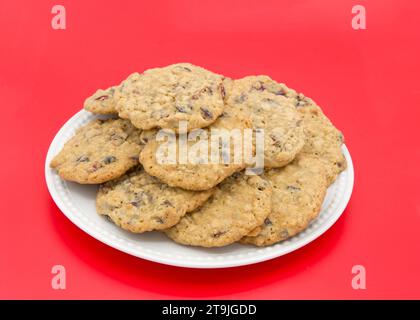 Nahaufnahme auf einer Porzellanplatte voller Haferflocken Cranberry-Kekse auf rotem Hintergrund. Stockfoto