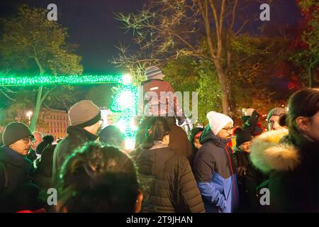 Ein Kind wird an einem Winterabend in Rathause, Wien, Österreich, inmitten der Massen von Weihnachtsmarktbesuchern auf der Schulter seines Vaters getragen Stockfoto