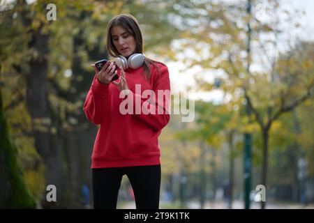 Sportliche Frau überprüft das Smartphone, bevor sie einige Übungen macht, hört Musik aus einer Playlist Stockfoto