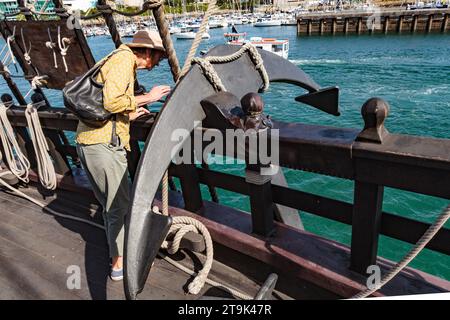 El Galeon Andalucía: Plymouth Barbican 2023. Eine voll funktionsfähige Nachbildung einer Galeone aus dem 16. Bis 17. Jahrhundert. Frau neben dem Schiffsanker Stockfoto