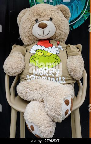 Lustiger Bär zu Weihnachten gekleidet mit dem Grinch Merry Christmas T-Shirt auf einem Stuhl Stockfoto
