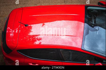 Rotes, normales Auto von oben, auf der Straße geparkt. Hardtop des roten Autos. Dach in Metallic-Rot mit getönten schwarzen Glasfenstern Stockfoto