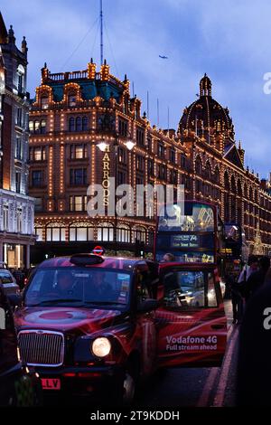 Knightsbridge an einem frühen Winterabend mit Harrods im Hintergrund und einem roten Taxi mit offener Tür Stockfoto