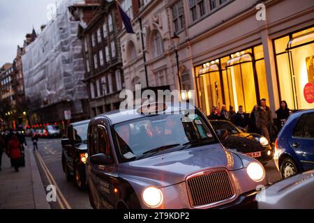 London Taxi fährt nachts durch die Regent Street in London, wo Geschäfte beleuchtet sind und die Leute während der Hauptverkehrszeit im Jahr 2013 im Hintergrund verschwimmen Stockfoto