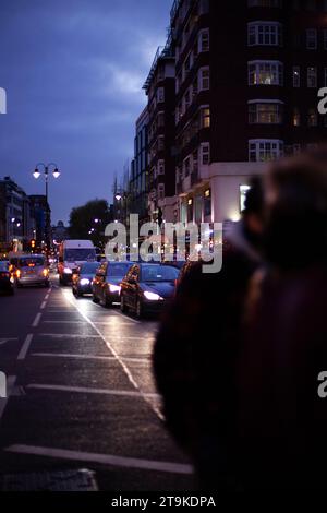 Knightsbridge mit Personen, die die geschäftige Straße nachts voller Verkehr verdecken, mit Lancelot Place Straßenschild im Hintergrund während der Hauptverkehrszeit Stockfoto