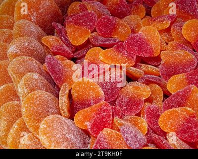 Eine Nahaufnahme von orangen und roten gummiartigen Bonbons in Form von Herzen, bedeckt mit Zuckerkristallen. Stockfoto