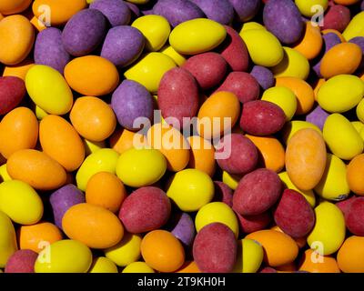 Eine Nahaufnahme eines Stapels farbenfroher, mit Süßigkeiten überzogener Pralinen in lila, gelb, orange und rot. Sie sind länglich und haben eine glatte Textur. Stockfoto