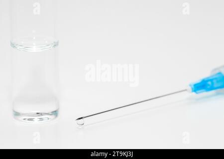 Spritzennadel mit Tropfen flüssiger Medizin, Ende und Glasampulle, Nahaufnahme Makroaufnahme, selektiver Fokus Stockfoto