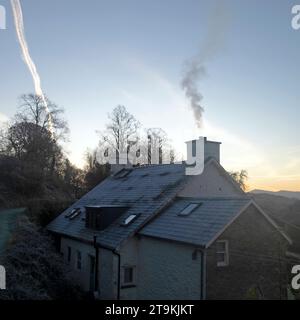 Rauch steigt aus einem Landhaus Haus im Winter und Dampfspur aus dem Flugzeug im Winter Morgen blauer Himmel ländliches Wales UK KATHY DEWITT Stockfoto