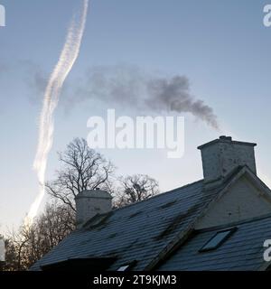 Rauch steigt aus einem Landhaus Haus im Winter und Dampfspur aus dem Flugzeug im Winter Morgen blauer Himmel ländliches Wales UK KATHY DEWITT Stockfoto