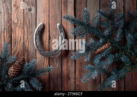 Altes Hufeisen und blaue Fichtenzweige mit Kegeln auf einem alten hölzernen Hintergrund. Das Konzept von froher Weihnachten und Neujahr. Stockfoto