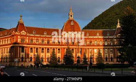 Die Menschen laufen in der Nähe des Bezirksrates Brasov, Consiliul Județean Brașov, das Gebäude, wenn die Sonne am 2. August 2023 in Brașov, Rumänien, untergeht. Foto von Tim Chong Stockfoto