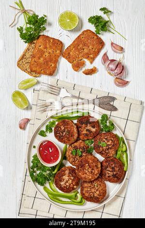 deutsche Frikadellen vom Rind- und Schweinefleisch, Semmelbrösel, Zwiebeln und Gewürze auf Teller mit Tomatensauce, Petersilie, grünen Pfefferscheiben auf weißem Holzta Stockfoto