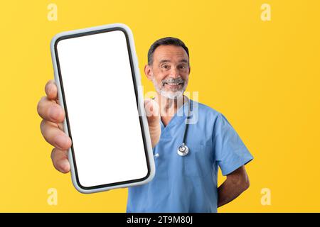 Reifer medizinischer Arbeiter Mann in Uniform, der Smartphone-Bildschirm demonstriert, Studio Stockfoto
