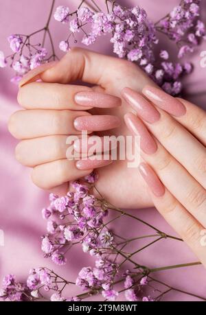 Weibliche Hände mit schöner Maniküre mit Gipsofila-Blüten auf rosa Seide Stockfoto