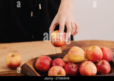 Weibliche Hände arrangieren eine Auswahl reifer roter Äpfel auf einem Holzbrett, symbolisieren die nährenden Entscheidungen eines gesunden Lebensstils, vegetarische Werte, a Stockfoto