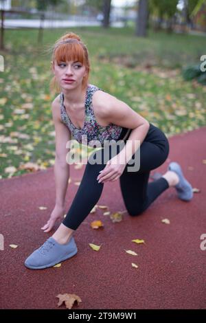 Junge rothaarige Kaukasierin in Sportbekleidung, bevor sie im Herbst auf die Laufbahn startet Stockfoto