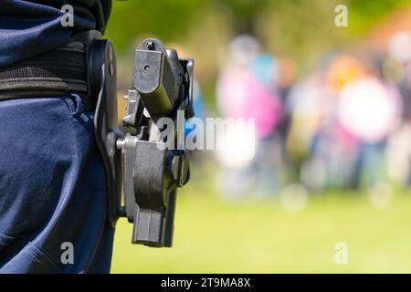 Automatische Polizeipistole auf der Seite eines Polizisten in blauer Uniform mit verschwommenem Hintergrund Stockfoto