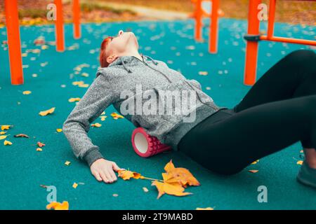 Junge kaukasische Stadtfrau mit Schaumwalze im Herbst nach dem Training im Park Stockfoto