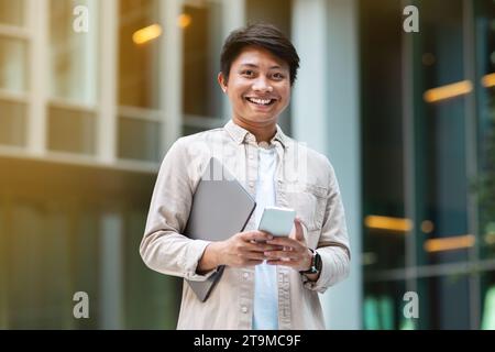 Junger asiatischer Unternehmer mit Laptop mit Smartphone Stockfoto