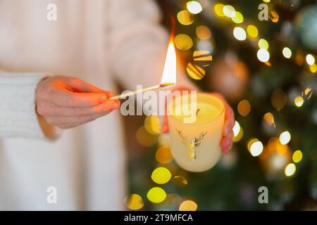 Die Frau überreicht eine große goldene Kerze mit Streichhölzern im Weihnachtskranz. Stockfoto