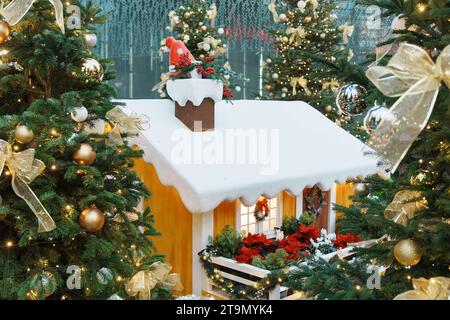 Ein festliches Bild eines traditionellen Weihnachtsbaums, umgeben von Geschenken und einem Miniaturpuppenhaus, beleuchtet von einem warmen, goldenen Licht Stockfoto