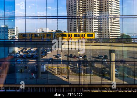 Reflexion des Detroit People Mover. Es handelt sich um ein 4,7 Kilometer langes, automatisch betriebenes Hochbahnsystem durch die Innenstadt von Detroit. Passagiere auf der Ringlinie sind Touristen und Mitarbeiter aus den Geschäften und Büros im Stadtzentrum. Die Fahrt kostet ein Viertel und bietet einen interessanten Blick auf die Gebäude im Zentrum von Detroit. Personenzug spiegelt sich in einer Glasfassade. Der erhöhte Peoplemover schlängelt sich seinen Weg durch die Innenstadt von Detroit, USA Stockfoto