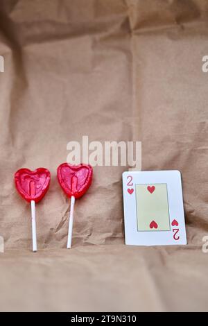 Zwei rote herzförmige Lutscher und eine zwei-Herzen-Karte auf Papphintergrund. Stockfoto