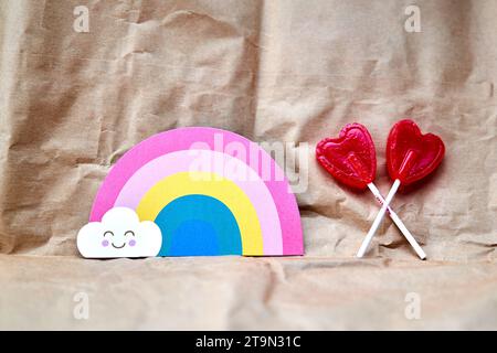 Zwei rote Herzlutscher mit einer regenbogenförmigen Karte auf einem Papphintergrund. Stockfoto
