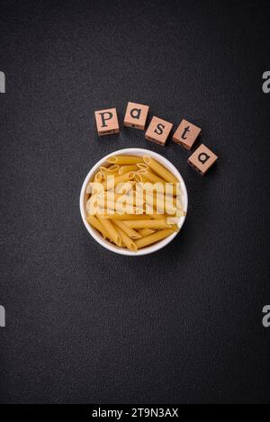 Rohe Penne-Pasta aus Vollkornweizensorten mit Salz und Gewürzen auf dunklem Betonhintergrund Stockfoto