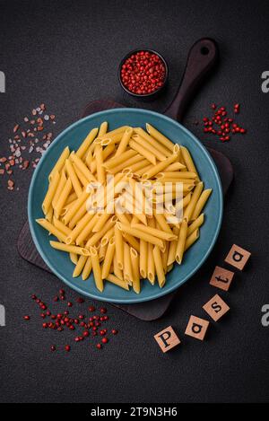 Rohe Penne-Pasta aus Vollkornweizensorten mit Salz und Gewürzen auf dunklem Betonhintergrund Stockfoto