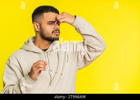 Erschöpfter, müder indischer Hindu-Mann zieht die Brille aus, spürt Augenschmerzen, ist überlastet Burnout durch lange Arbeitszeiten. Verschlafener, erschöpfter Arabianer, der die Augen isoliert auf gelbem Hintergrund reibt Stockfoto