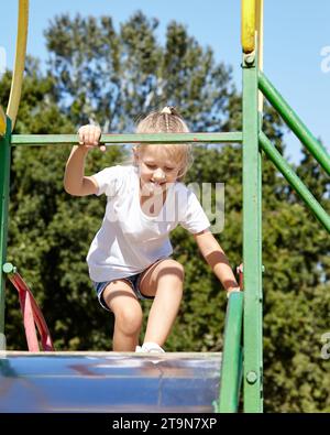 Kleines Mädchen, das auf einer Rutsche auf einem Spielplatz im Sommer-Stadtpark spielt. Kindheit, Freizeit und Menschenkonzept - glückliche Kinderruhe und viel Spaß Stockfoto