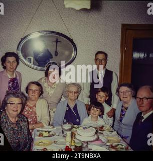 Eine Großfamilie, die 1962 Geburtstag feiert. Es gibt vier Generationen von Familien, die um einen Tisch sitzen. Das Foto zeigt einen Speisesaal aus den 1960er Jahren, Mode aus den 1960er Jahren und einen Nachmittagstee mit Salat, Blancmange und Kuchen. Dies ist ein Foto, das von der Originalfolie aufgenommen wurde. Stockfoto