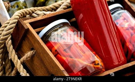 Glas Gläser mit eingelegten roten Paprika und Flaschen mit Tomatensoße in einer rustikalen Zusammensetzung isoliert. Gläser mit einer Vielzahl von eingelegten Gemüse vor Stockfoto