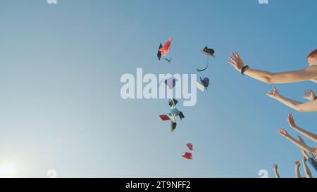 Absolventen werfen bunte Hüte gegen einen blauen Himmel. Stockfoto