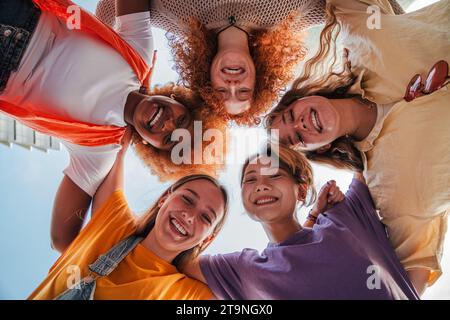 Tiefwinkelansicht von fünf Teenagern, die lachen und in die Kamera schauen. Eine Gruppe junger Frauen, die lächelnd nach unten schauen. Echte sorglose Damen, die sich zusammen umarmen. Begeisterte Freunde posieren für ein Foto-Porträt. Hochwertige Fotos Stockfoto