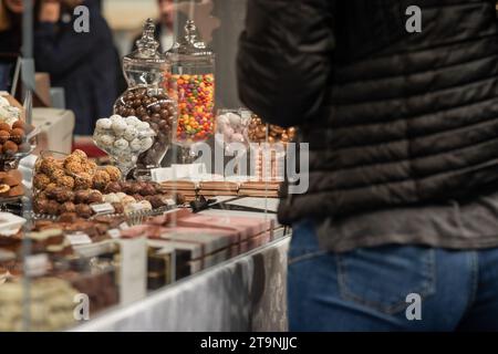 Person, die verschiedene Arten von Süßigkeiten auf einem Display auswählt. Viele Pralinen auf einem schönen, sichtbaren Rücken einer unbekannten Frau in Jeans. Stockfoto