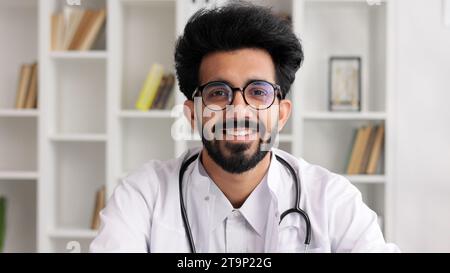 Porträt eines jungen indischen Arztes, der lächelt und die Kamera in einem weißen Mantel mit Stethoskop anschaut. Nahansicht. Stockfoto