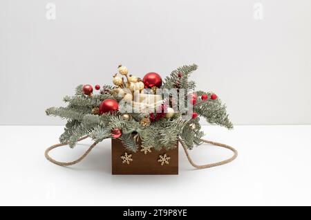 Weihnachtsstrauß aus Tannenzweigen, goldenen und roten Ornamenten in Holzkiste auf weißem Hintergrund. Neujahrsdekoration. Stockfoto