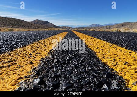 Nahaufnahme einer abgelegenen Straße und gelben Linien, die in entfernte Berge führen Stockfoto