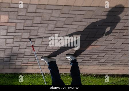 Eine gesichtslose blinde Frau läuft mit einem Stock die Straße entlang. Stockfoto