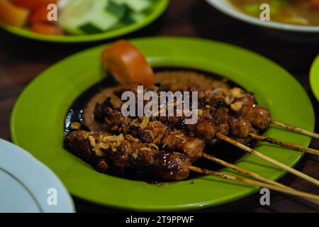 Traditioneller indonesischer Satay oder Sate mit Erdnusssauce, Sojaketchup-Tomatenscheibe und gebratenen Zwiebeln als Topping. Stockfoto