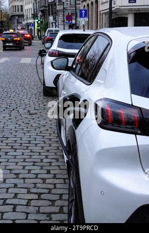 Vertikale Nahaufnahme von zwei weißen Elektroautos, die in den coble-Steinstraßen von Brüssel aufladen Stockfoto