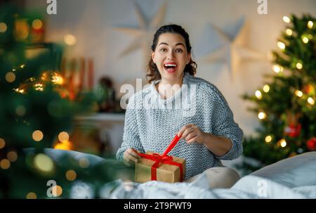 Frohe Weihnachten, Frohe Feiertage. Überraschte Happy Woman, die ein Weihnachtsgeschenk öffnet. Stockfoto