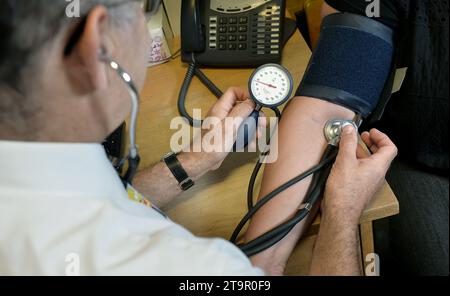 Aktenfoto vom 09/14 eines Hausarztes, der den Blutdruck eines Patienten überprüft. Ein System, das den Zugang zur Allgemeinpraxis durch die Einbeziehung von Mitarbeitern wie Apothekern und Ärztinnen und Ärzten verbessert, könnte dazu führen, dass freie Stellen in der Allgemeinpraxis reduziert werden, so eine neue Umfrage. Ausgabedatum: Montag, 27. November 2023. Stockfoto