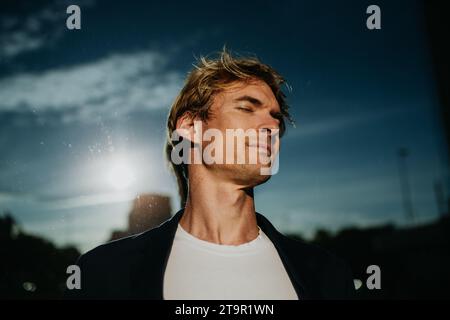 Porträt eines gutaussehenden reifen Mannes mit blonden Haaren und geschlossenen Augen, der draußen vor einer reflektierenden Wand steht. Stockfoto