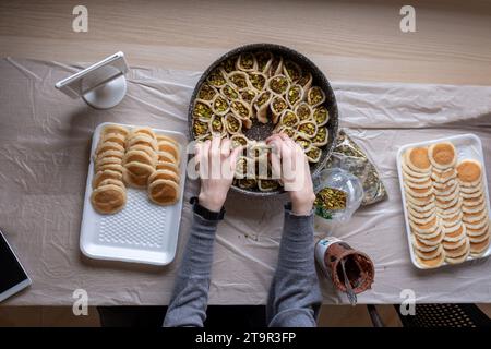 Hände halten Qatayef gefüllt mit Schokolade und mit Pistazien belegt auf einem Holztisch, mit einem Teller, der später im Ofen als Ramadan swe zubereitet wird Stockfoto