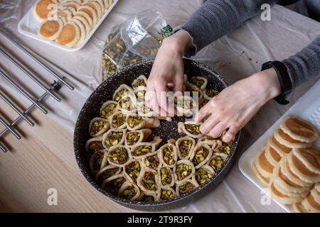 Hände halten Qatayef gefüllt mit Schokolade und mit Pistazien belegt auf einem Holztisch, mit einem Teller, der später im Ofen als Ramadan swe zubereitet wird Stockfoto