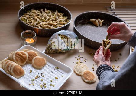 Hände halten Qatayef gefüllt mit Schokolade und mit Pistazien belegt auf einem Holztisch, mit einem Teller, der später im Ofen als Ramadan swe zubereitet wird Stockfoto